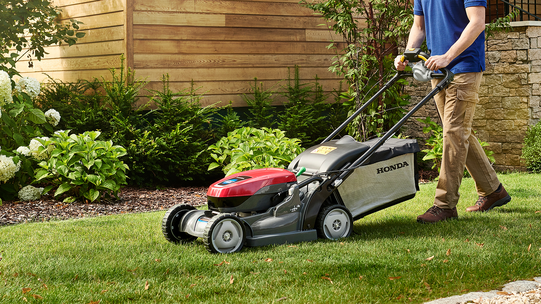 Mann beim Schieben eines HRX-Akkurasenmähers in einem Garten.